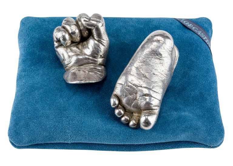 Starling silver casts of a baby's clenched hand and foot showing the detail on the sole. Placed on a teal cushion